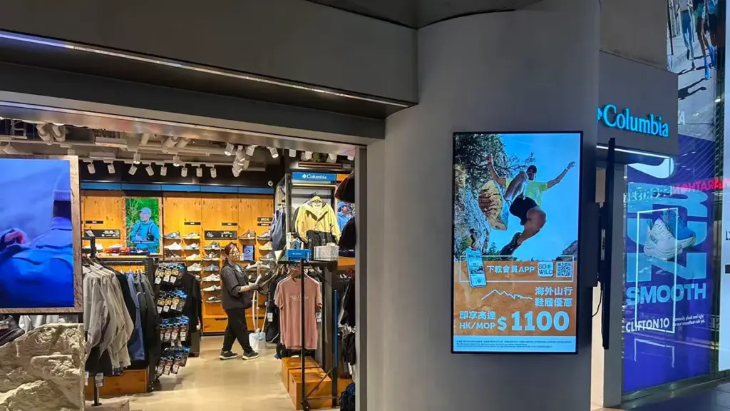 A vertical digital advertising display mounted outside a retail store