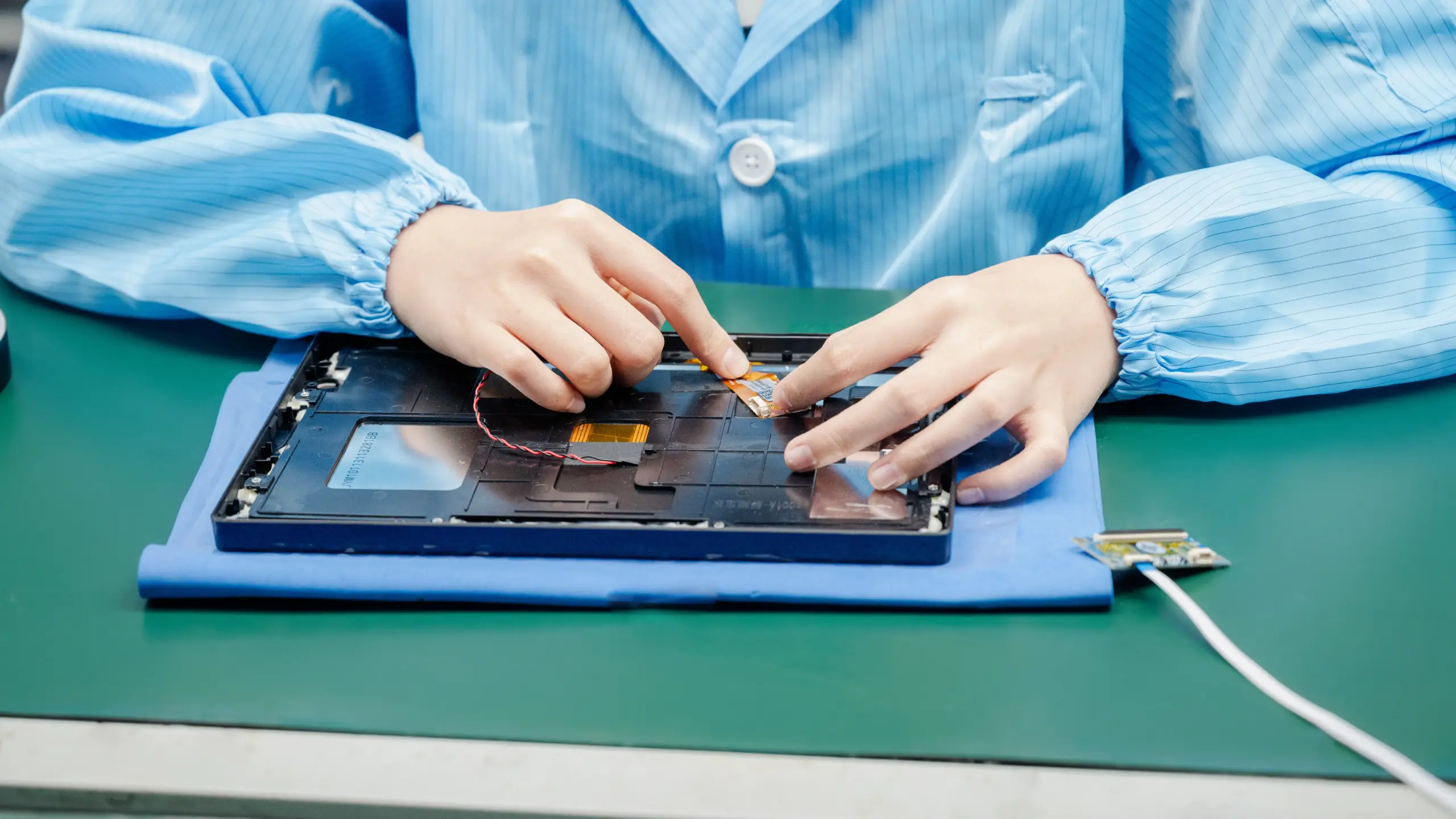 Electronics Assembly Workstation for Device Manufacturing Worker in blue anti-static uniform assembling electronic device components at a green workstation bench