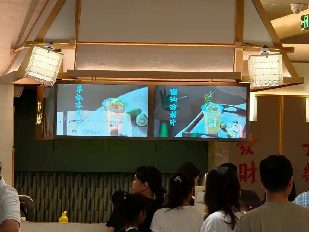 Customers queue at a counter beneath digital screens displaying beverage menus with Chinese characters